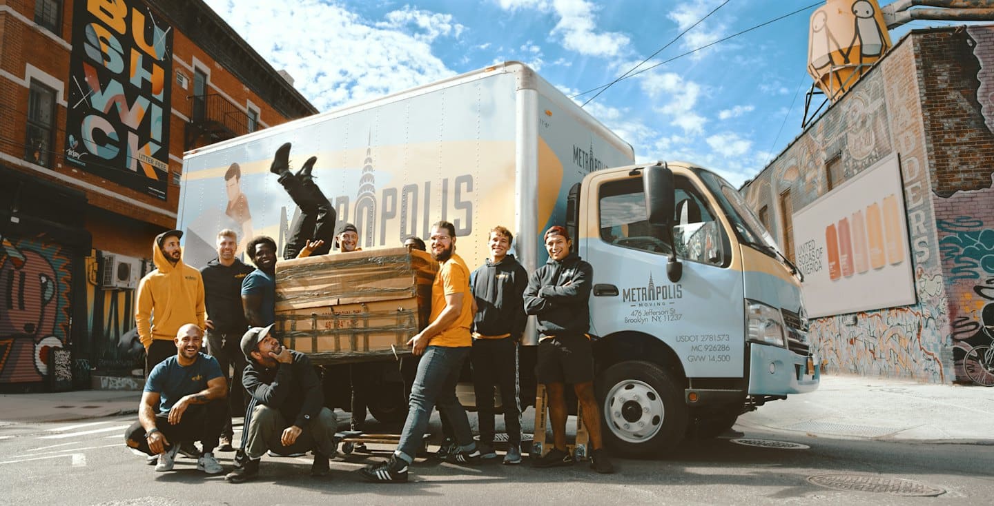 Home Movers in branded attire posing by their truck on a city street.